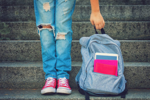 child wearing ripped jeans and red lace ups with a blue rucksack containing books to illustrate back to school