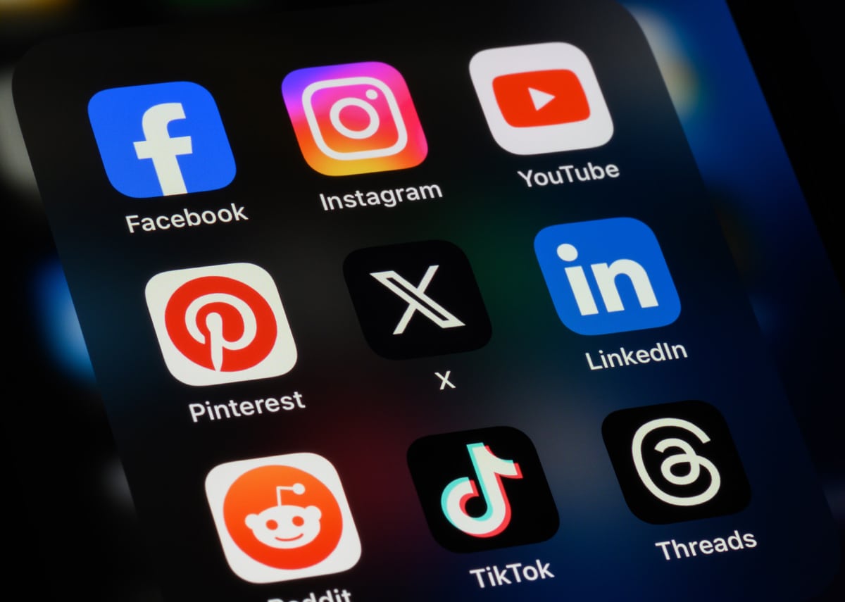 Smartphone screen displaying popular social media app icons, including Facebook, Instagram, YouTube, Pinterest, X, LinkedIn, Reddit, TikTok, and Threads, on a dark background.