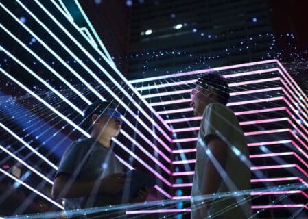 Two people wearing AR glasses standing in a futuristic digital environment with neon grid lines and data-like visual effects, symbolising immersive technology and virtual experiences.