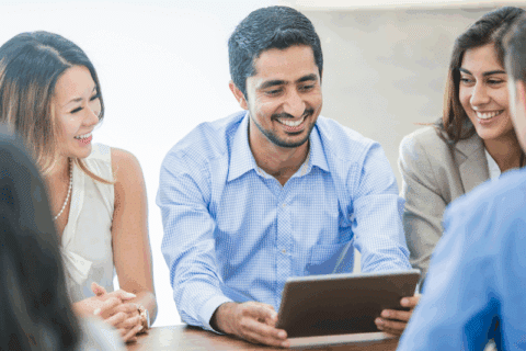 Group of professionals smiling and discussing work around a tablet during a meeting, representing collaboration and communication in science marketing.